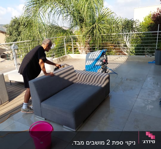 אדם מנקה ספה עם מכשיר ניקוי על מרפסת